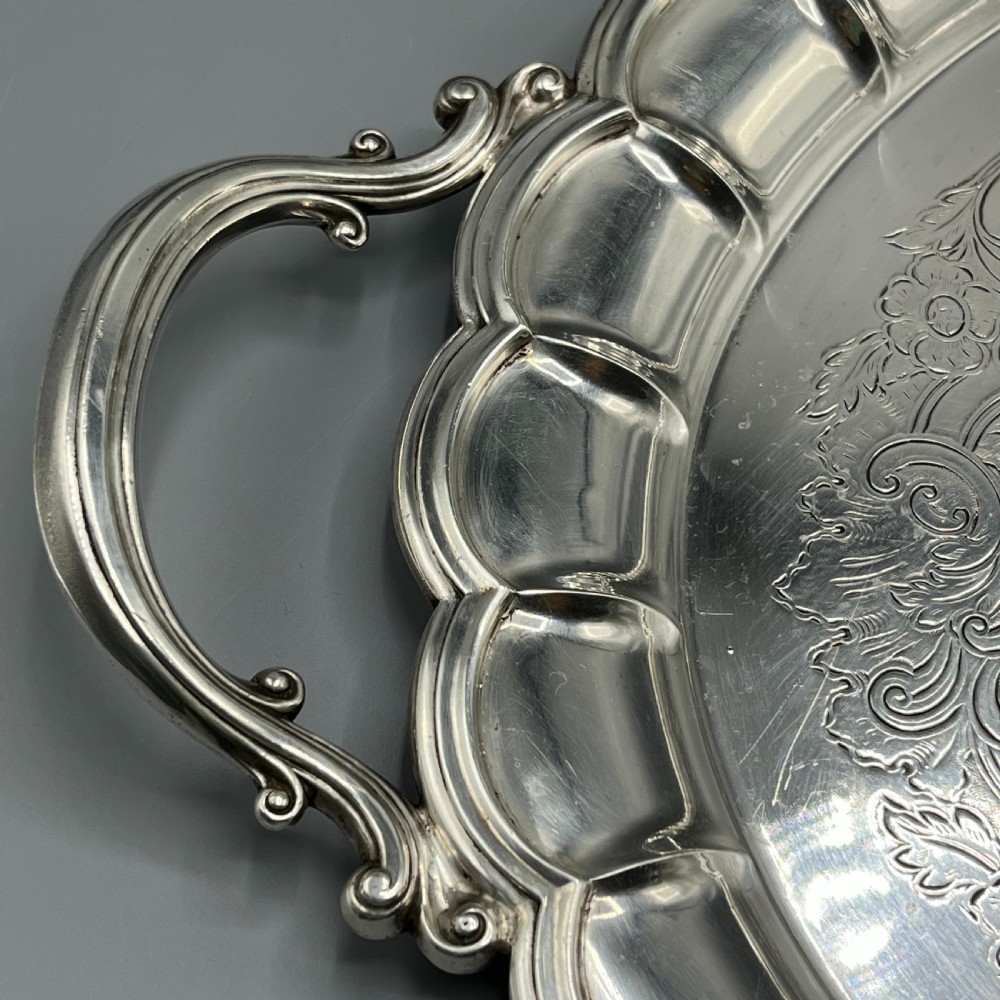 A large oval silver plated serving tray featuring twin scroll handles, a scalloped rim, and chased foliage patterns across the flat interior. View VI