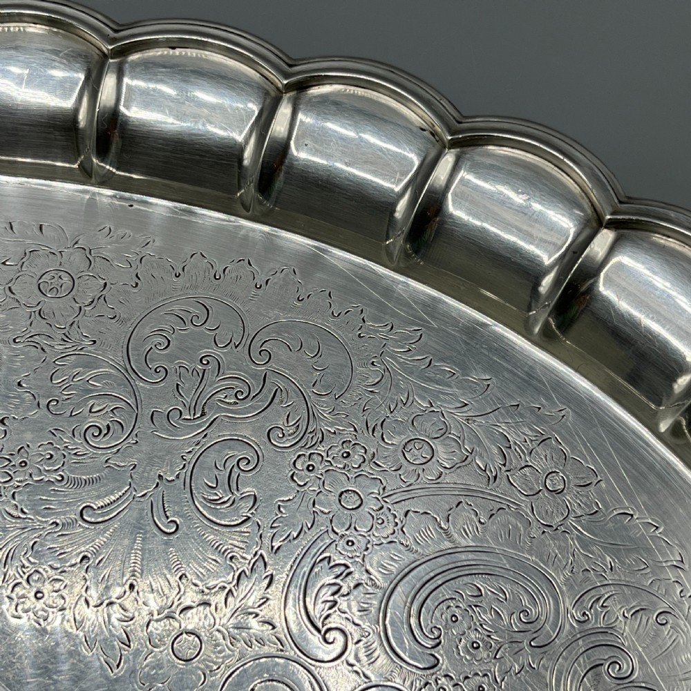 A large oval silver plated serving tray featuring twin scroll handles, a scalloped rim, and chased foliage patterns across the flat interior. View X