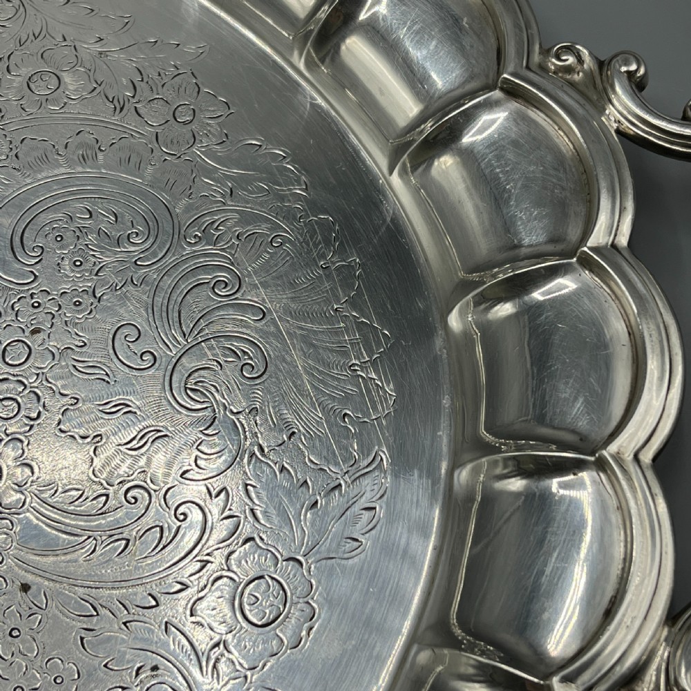 A large oval silver plated serving tray featuring twin scroll handles, a scalloped rim, and chased foliage patterns across the flat interior. View XI