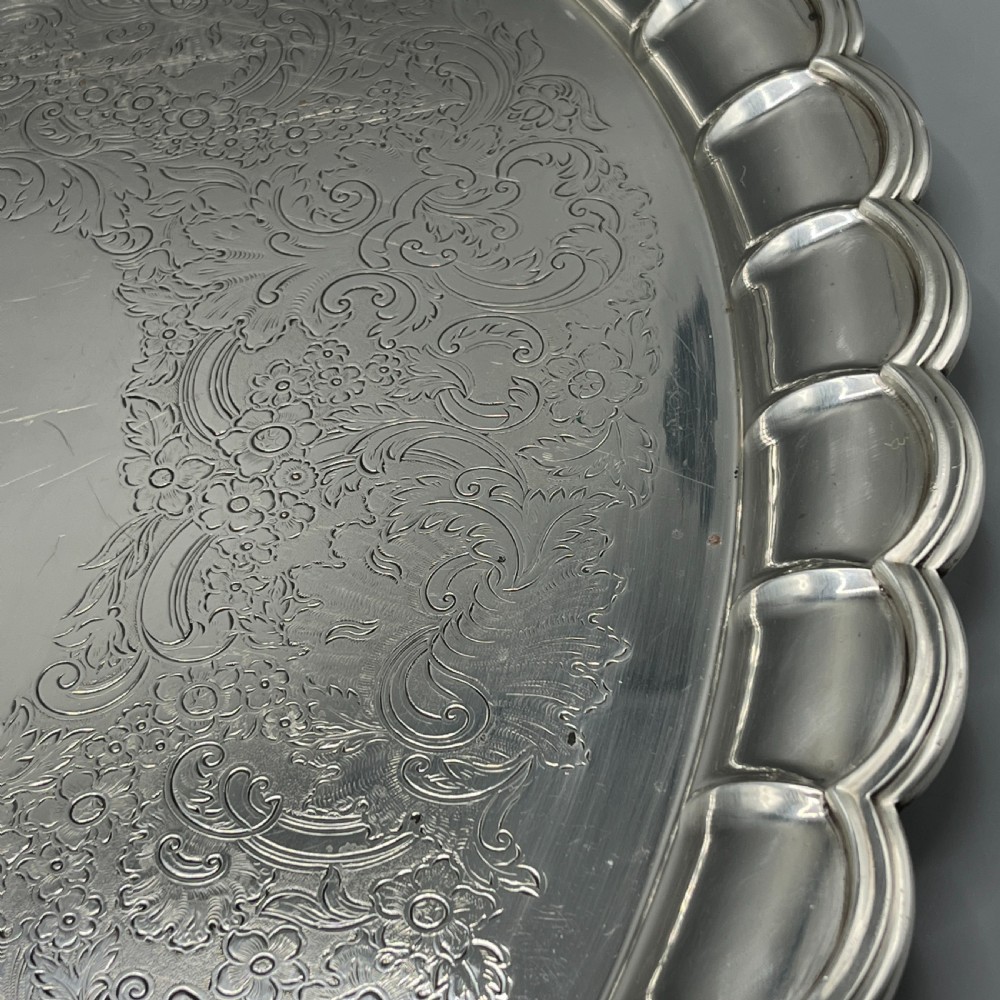 A large oval silver plated serving tray featuring twin scroll handles, a scalloped rim, and chased foliage patterns across the flat interior. View XIV