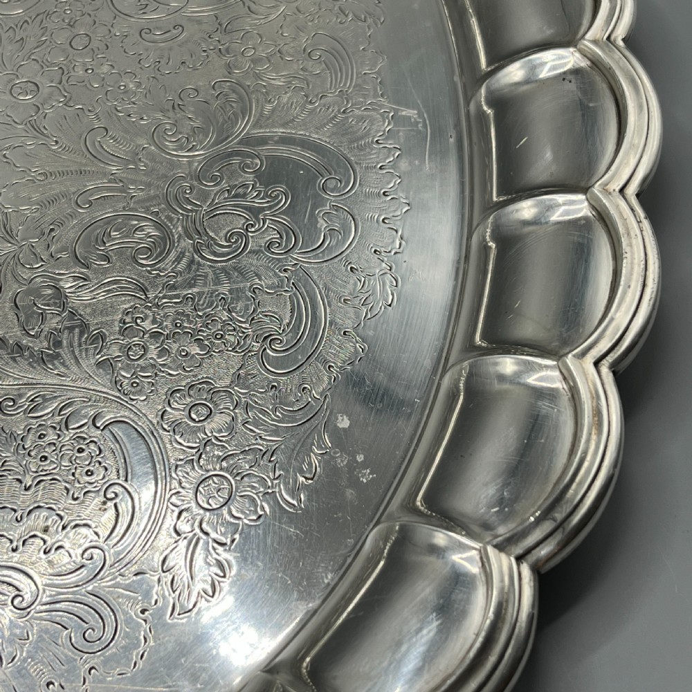 A large oval silver plated serving tray featuring twin scroll handles, a scalloped rim, and chased foliage patterns across the flat interior. View XV
