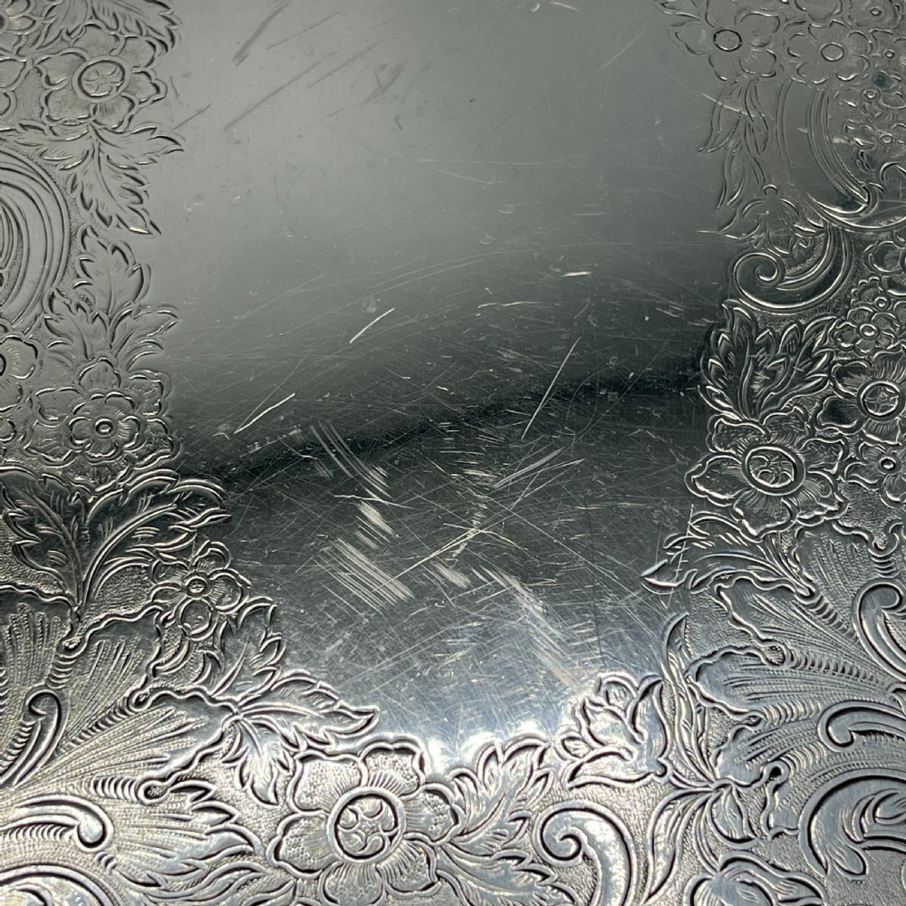 A large oval silver plated serving tray featuring twin scroll handles, a scalloped rim, and chased foliage patterns across the flat interior. View XVI