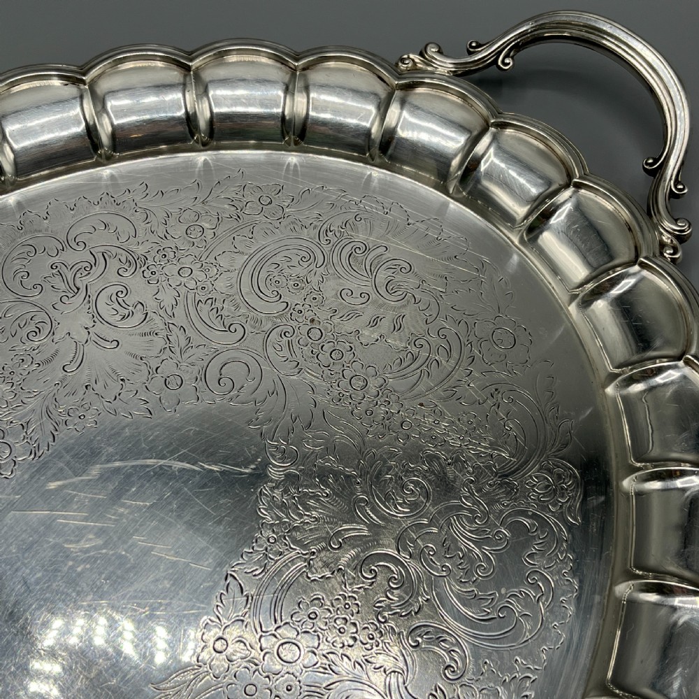 A large oval silver plated serving tray featuring twin scroll handles, a scalloped rim, and chased foliage patterns across the flat interior. View XVIII