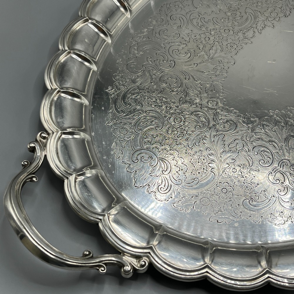 A large oval silver plated serving tray featuring twin scroll handles, a scalloped rim, and chased foliage patterns across the flat interior. View XIX