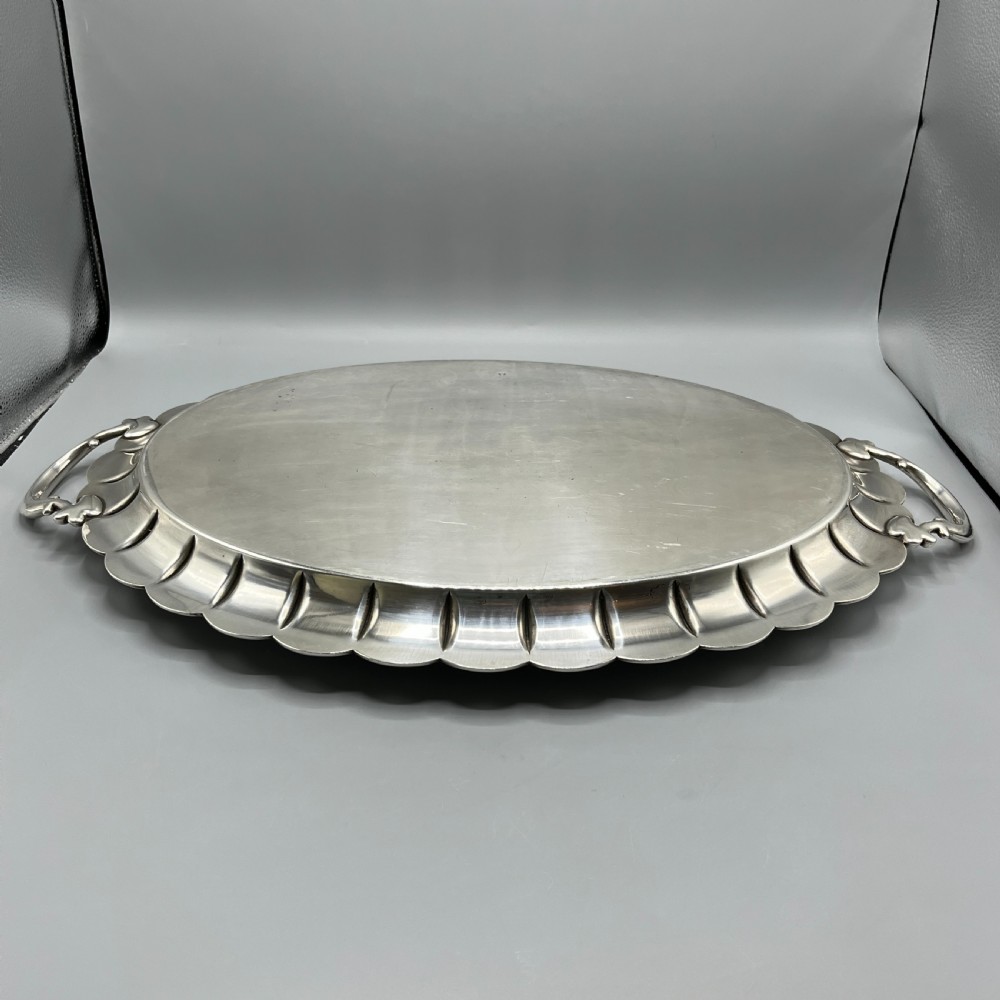 A large oval silver plated serving tray featuring twin scroll handles, a scalloped rim, and chased foliage patterns across the flat interior. View XX