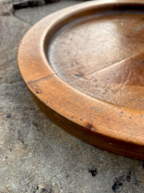 fig 3. A circular turned sycamore wooden platter featuring a raised rim, shallow basin with knife marks, and a dark triangular iron burn mark in the centre.