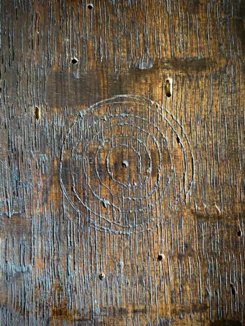 fig 1. A carved dark oak panel featuring a repetitive geometric foliage pattern beside a detailed close-up of incised concentric circles and ritual marks on the wood grain.