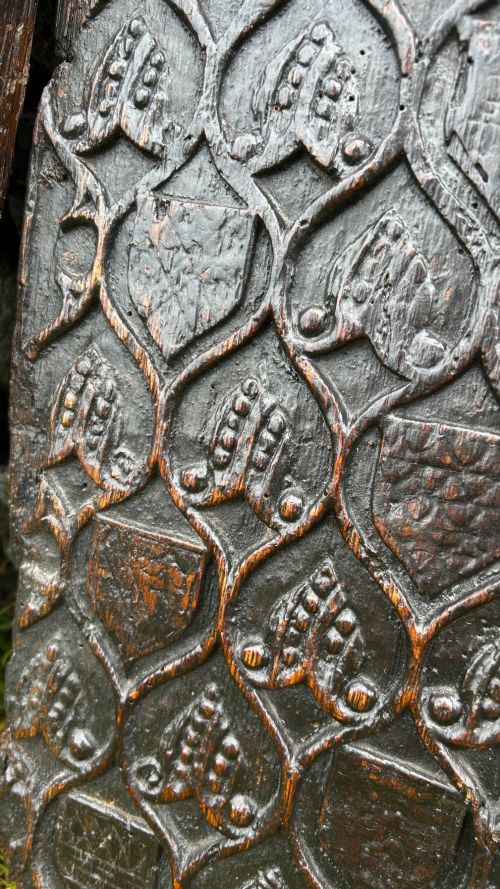 fig 6. A carved dark oak panel featuring a repetitive geometric foliage pattern beside a detailed close-up of incised concentric circles and ritual marks on the wood grain.