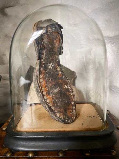 fig 1. A weathered nineteenth-century leather childs shoe sole mounted upright inside a glass display dome with an ebonised wooden base.