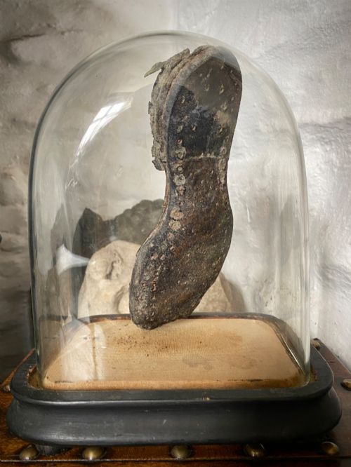 fig 2. A weathered nineteenth-century leather childs shoe sole mounted upright inside a glass display dome with an ebonised wooden base.