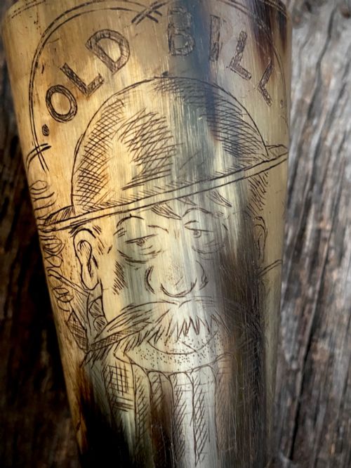fig 1. A translucent natural horn beaker featuring a detailed line engraving of the Bruce Bairnsfather character Old Bill wearing a helmet.