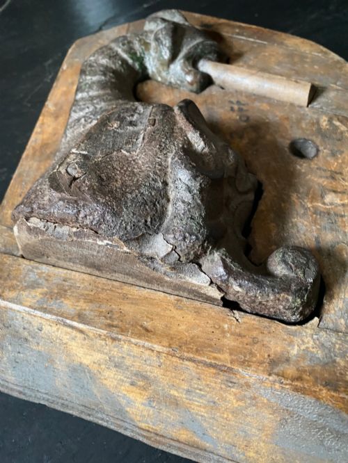 fig 2. A three-piece set of carved wooden pattern moulds featuring a central seated gargoyle figure flanked by two bat-like wing panels with red paint accents.
