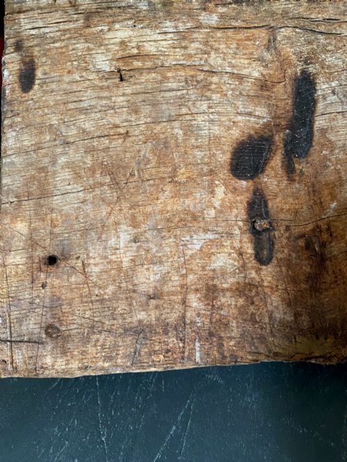 fig 3. A tall, hand-hewn 17th-century solid oak beam featuring multiple dark apotropaic taper burn marks along its weathered wood surface.