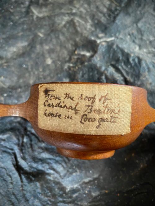 fig 1. A small carved wooden quaich featuring two side handles and an aged handwritten paper label attached to the front bowl.