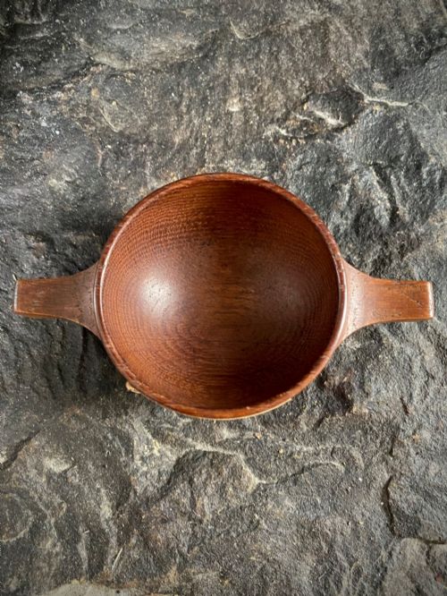 fig 2. A small carved wooden quaich featuring two side handles and an aged handwritten paper label attached to the front bowl.