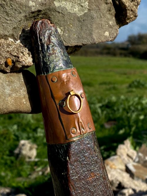 fig 1. A square-cut dark oak table leg featuring hand-carved lettering along its shaft and a brass collar at the tapered base.