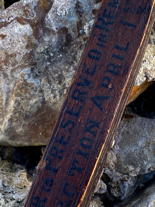 fig 4. A square-cut dark oak table leg featuring hand-carved lettering along its shaft and a brass collar at the tapered base.