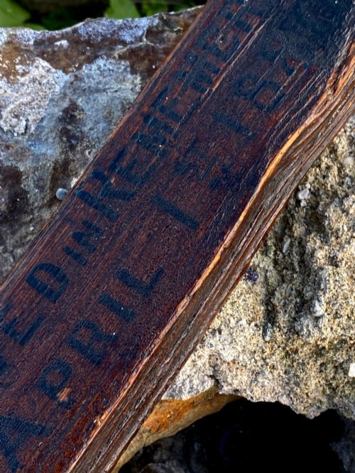 fig 5. A square-cut dark oak table leg featuring hand-carved lettering along its shaft and a brass collar at the tapered base.