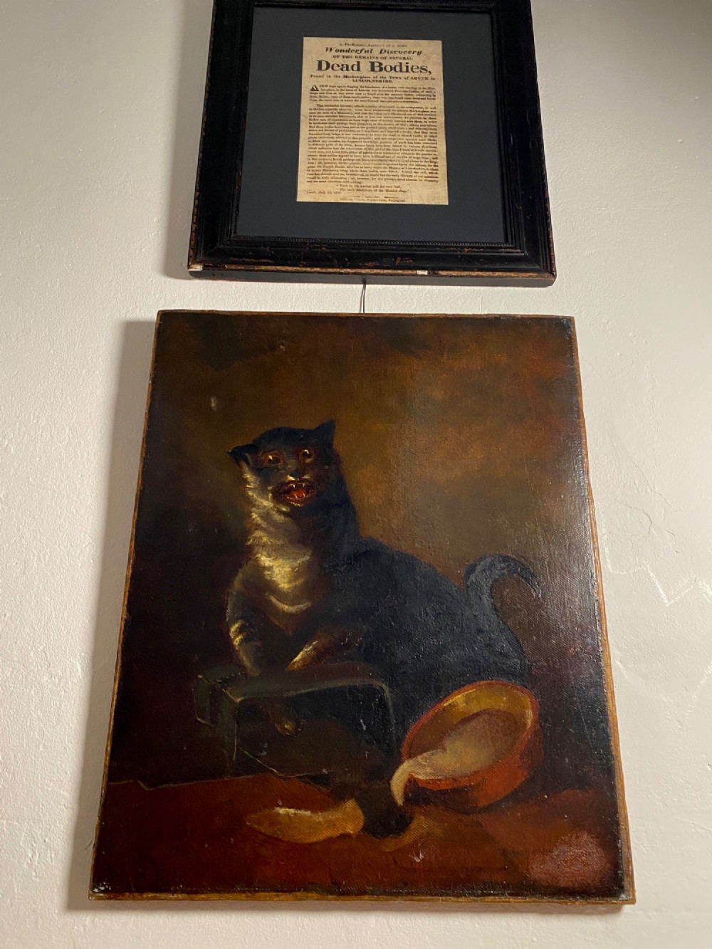A 19th-century unframed oil painting on canvas showing a dark cat positioned beside an overturned bowl on a dark background. View II