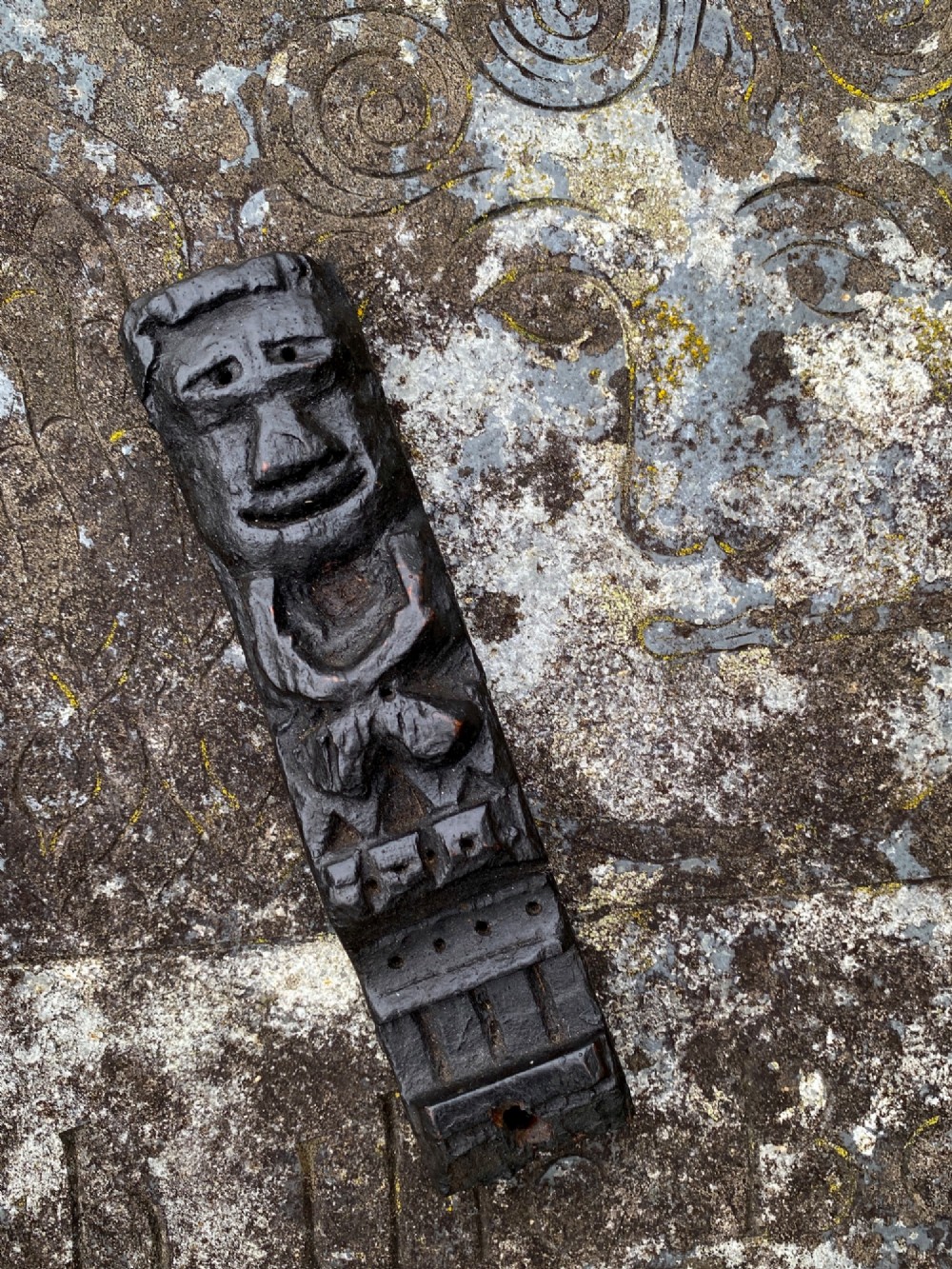 A dark carved oak wooden fragment depicting a stylized human face and decorative geometric relief details.