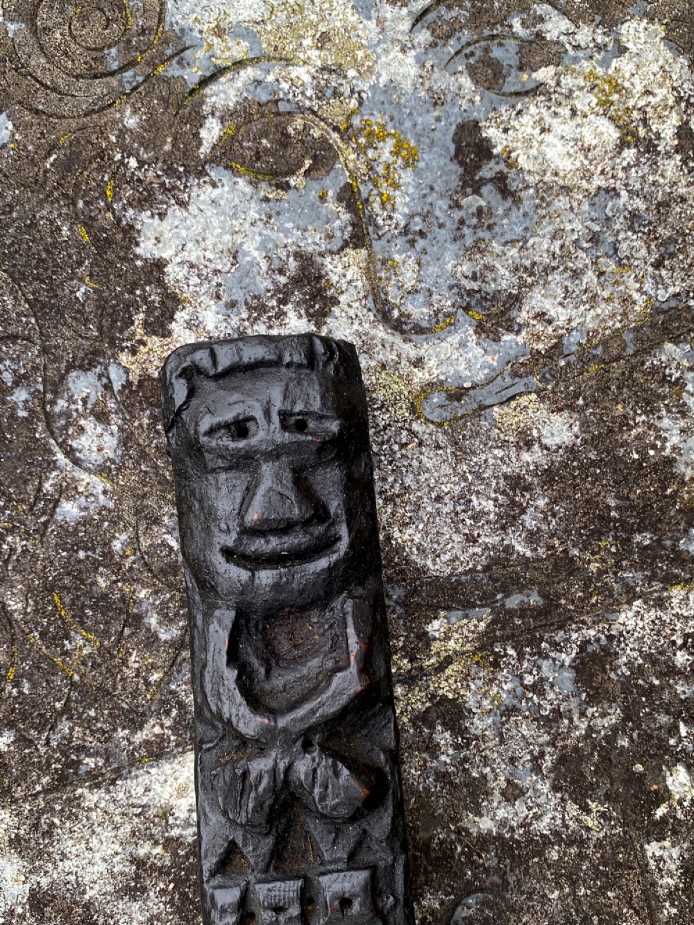 A dark carved oak wooden fragment depicting a stylized human face and decorative geometric relief details. View III