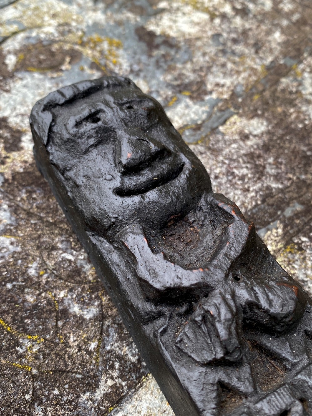 A dark carved oak wooden fragment depicting a stylized human face and decorative geometric relief details. View IV