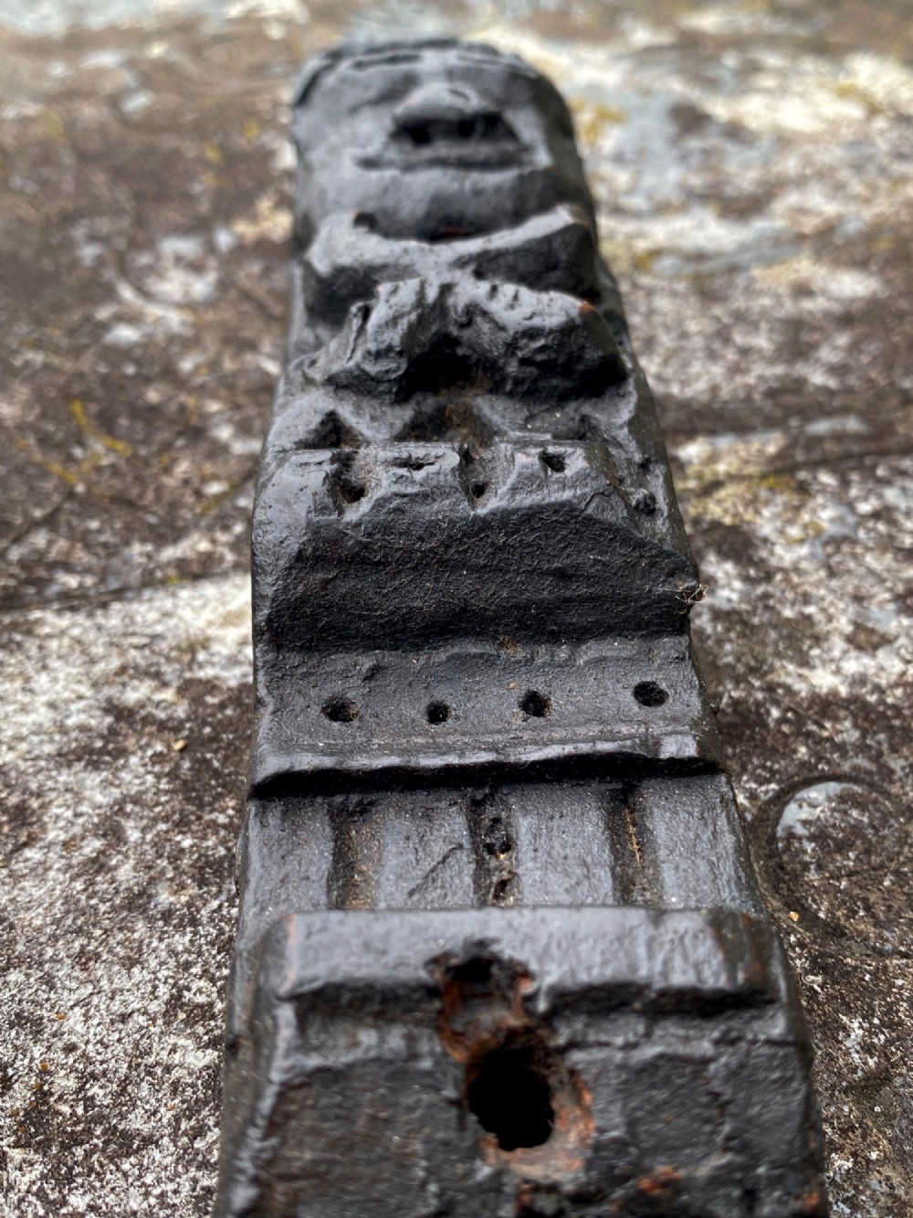 A dark carved oak wooden fragment depicting a stylized human face and decorative geometric relief details. View V