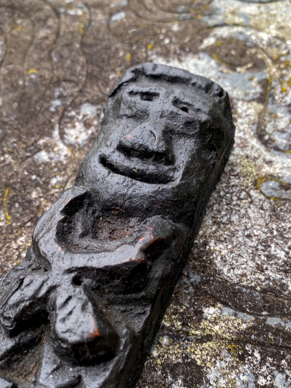 A dark carved oak wooden fragment depicting a stylized human face and decorative geometric relief details. View VI
