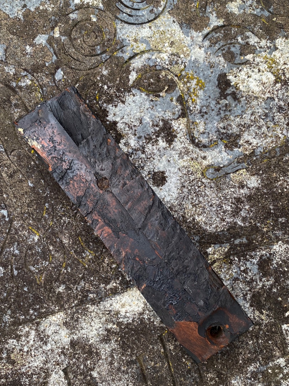 A dark carved oak wooden fragment depicting a stylized human face and decorative geometric relief details. View IX