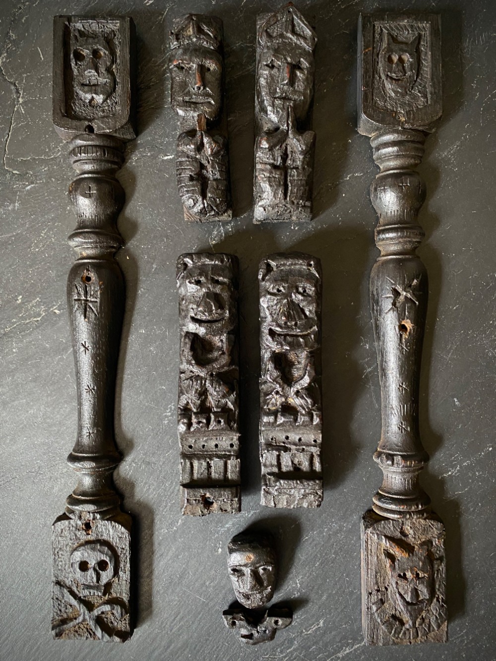 A dark carved oak wooden fragment depicting a stylized human face and decorative geometric relief details. View XII