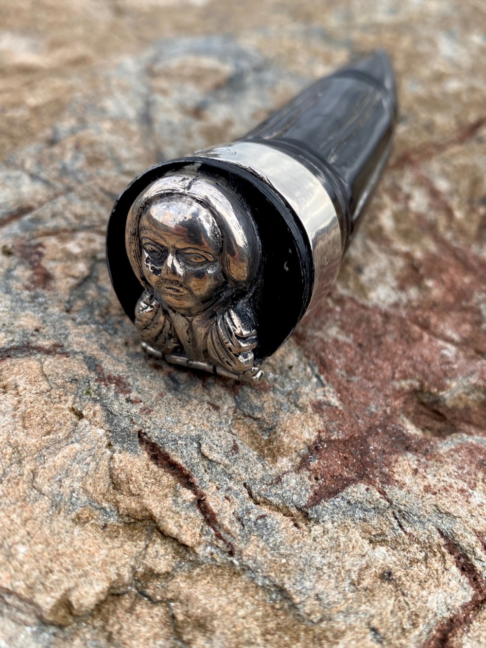 A 19th-century dark carved horn snuff mull featuring a sterling silver rim collar and a silver lid hinged with an allegorical face relief.