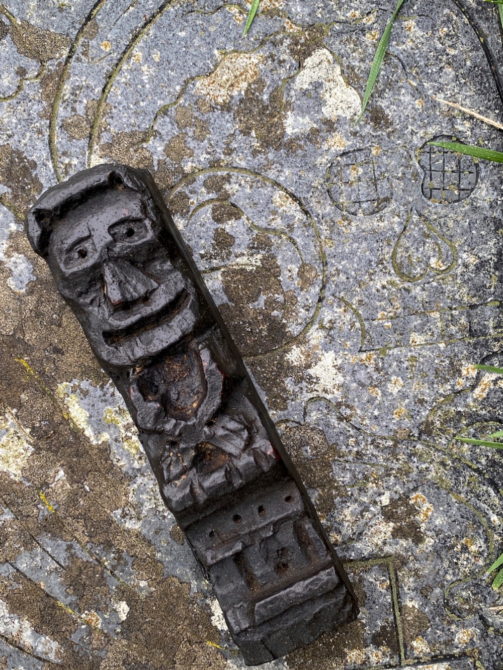 A vertical dark oak wood carving depicting a stylised human face and figure with hand-chiselled detailing.