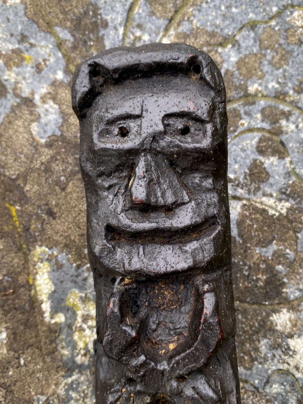 A vertical dark oak wood carving depicting a stylised human face and figure with hand-chiselled detailing. View V