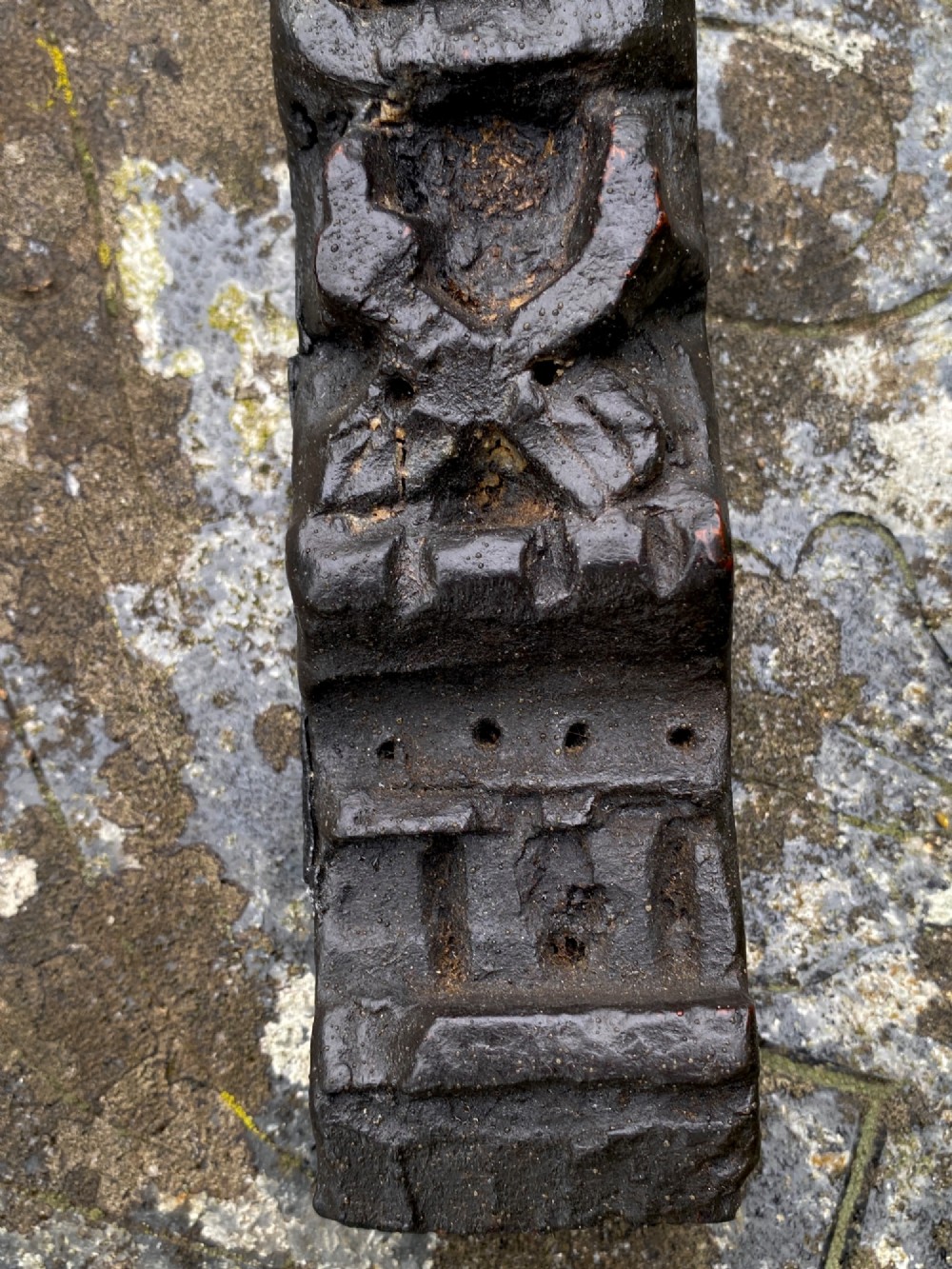 A vertical dark oak wood carving depicting a stylised human face and figure with hand-chiselled detailing. View VI