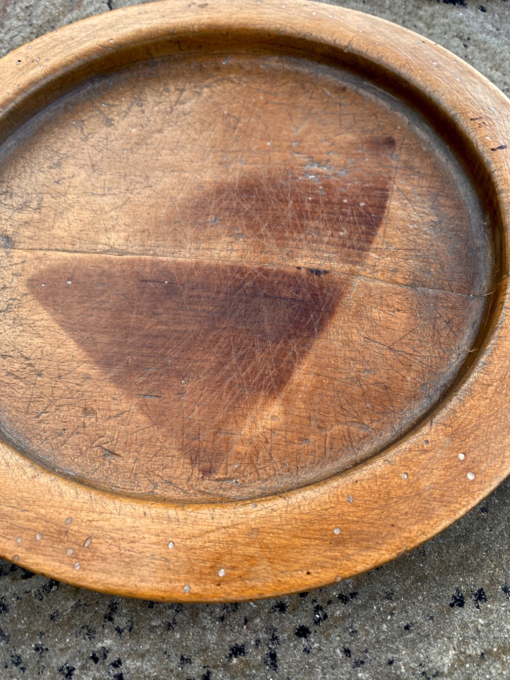A circular turned sycamore wooden platter featuring a raised rim, shallow basin with knife marks, and a dark triangular iron burn mark in the centre. View II