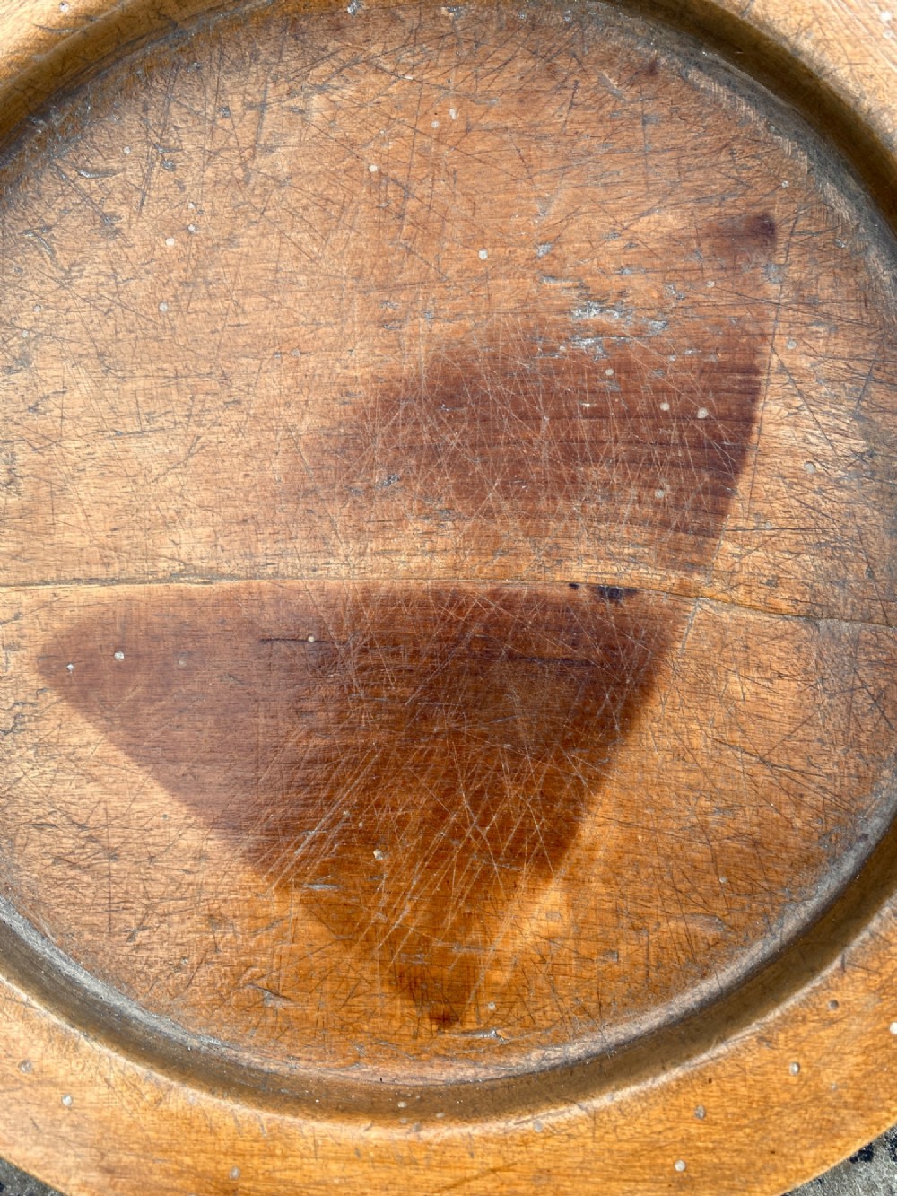 A circular turned sycamore wooden platter featuring a raised rim, shallow basin with knife marks, and a dark triangular iron burn mark in the centre. View III