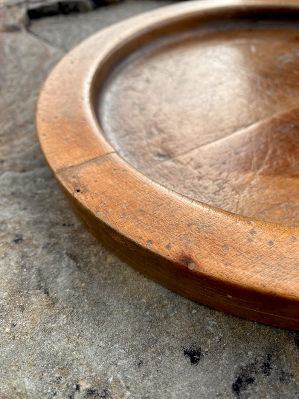 A circular turned sycamore wooden platter featuring a raised rim, shallow basin with knife marks, and a dark triangular iron burn mark in the centre. View IV