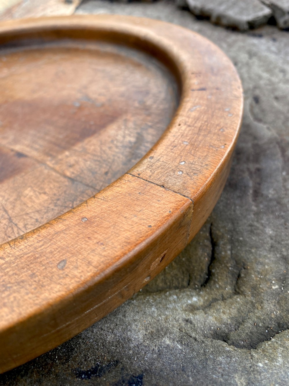 A circular turned sycamore wooden platter featuring a raised rim, shallow basin with knife marks, and a dark triangular iron burn mark in the centre. View V