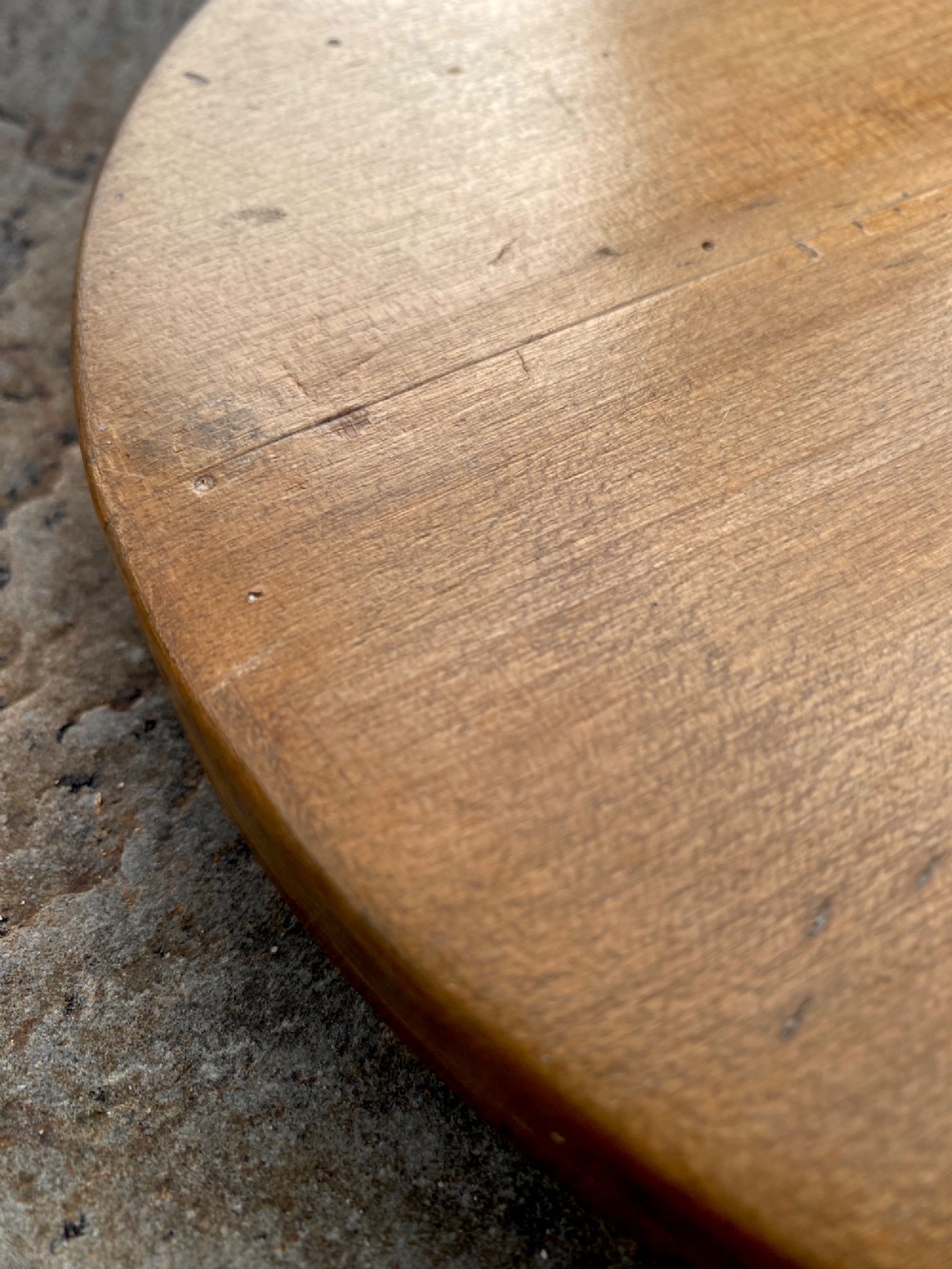 A circular turned sycamore wooden platter featuring a raised rim, shallow basin with knife marks, and a dark triangular iron burn mark in the centre. View VIII