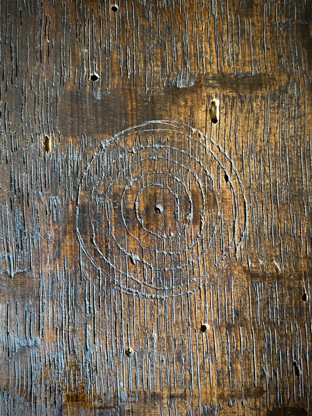 A carved dark oak panel featuring a repetitive geometric foliage pattern beside a detailed close-up of incised concentric circles and ritual marks on the wood grain. View II