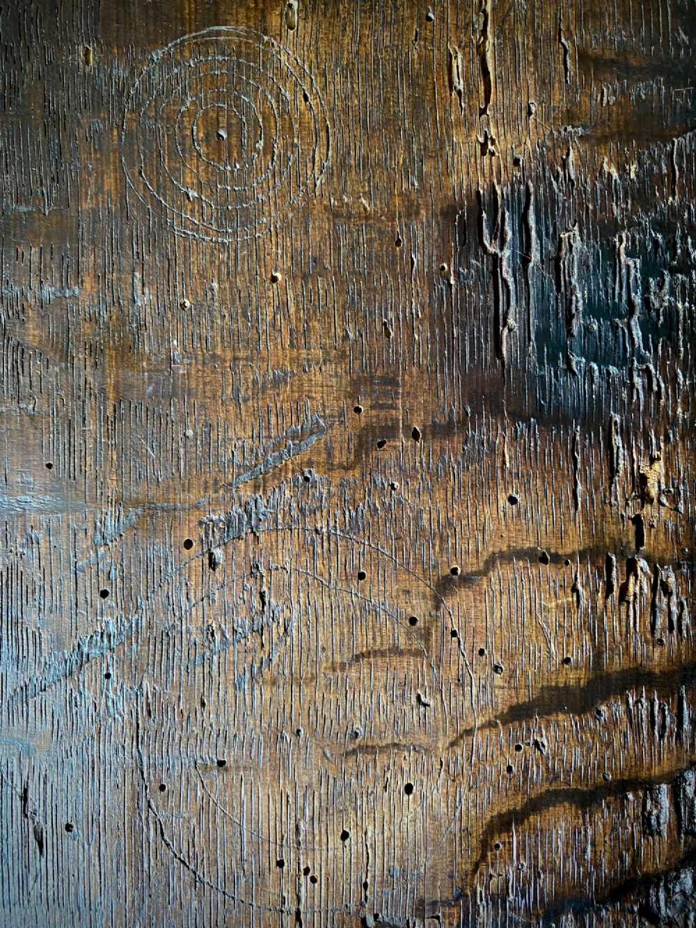 A carved dark oak panel featuring a repetitive geometric foliage pattern beside a detailed close-up of incised concentric circles and ritual marks on the wood grain. View V