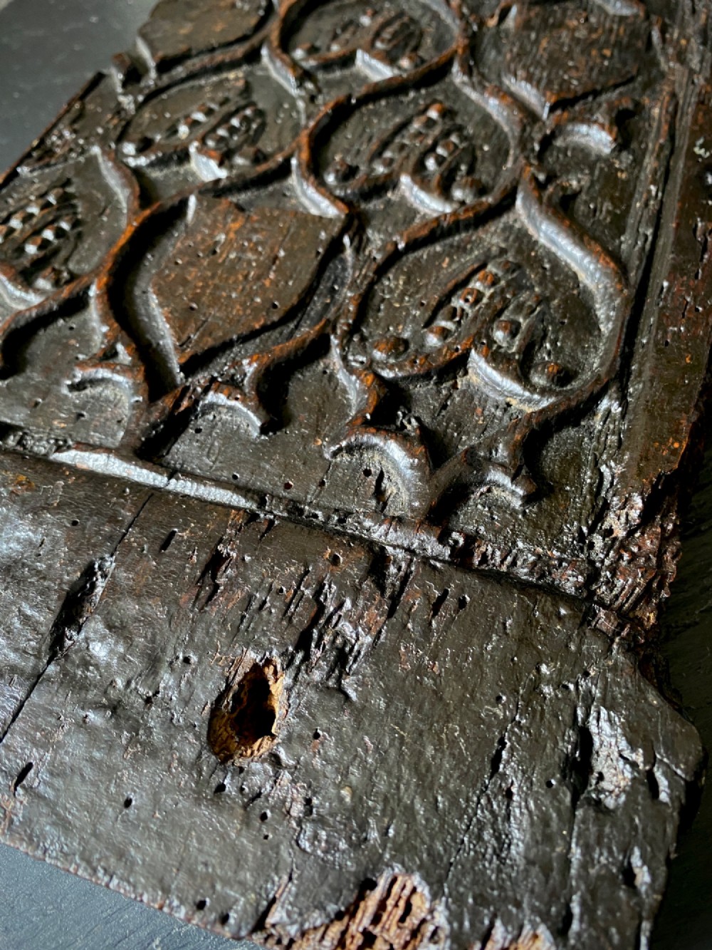 A carved dark oak panel featuring a repetitive geometric foliage pattern beside a detailed close-up of incised concentric circles and ritual marks on the wood grain. View XI