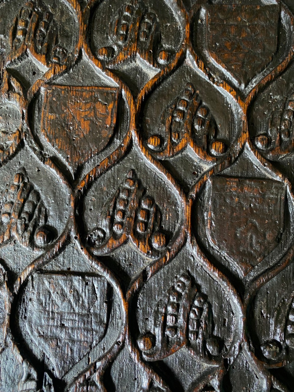 A carved dark oak panel featuring a repetitive geometric foliage pattern beside a detailed close-up of incised concentric circles and ritual marks on the wood grain. View XIV