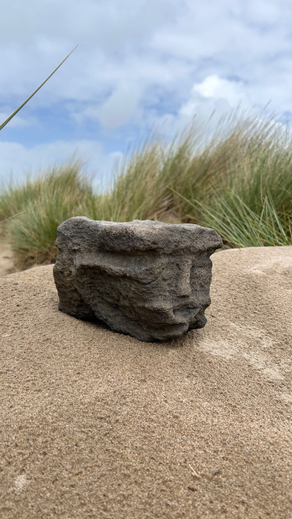 A hand-carved medieval grey stone corbel featuring a stylised human face with a gripping mouth detail. View VII