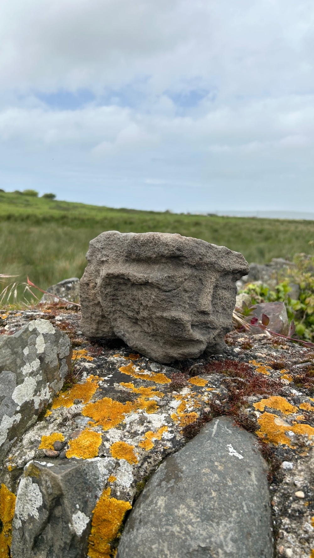 A hand-carved medieval grey stone corbel featuring a stylised human face with a gripping mouth detail. View IX