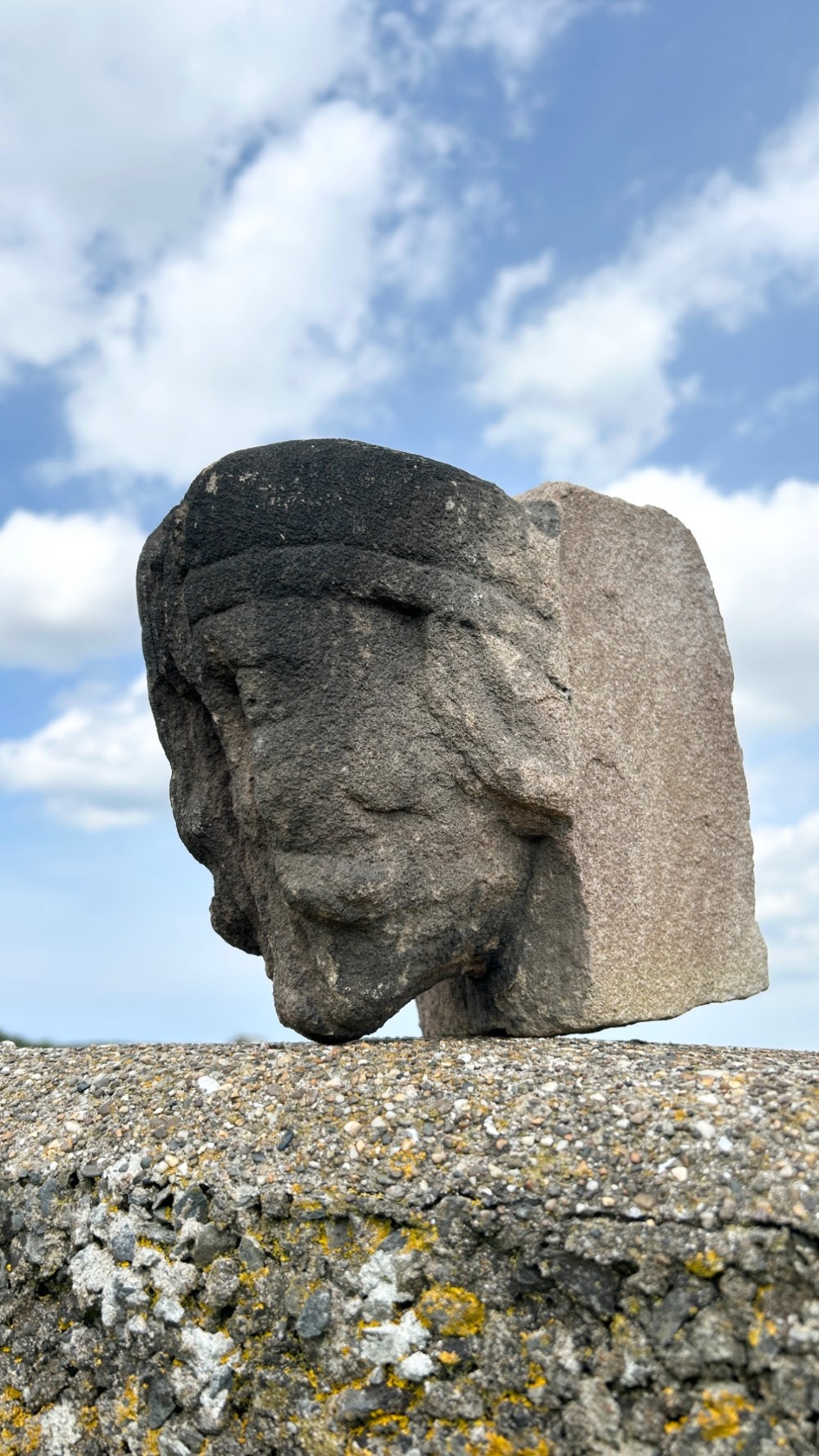 A weathered 17th-century carved stone head fragment with defined facial features and visible surface erosion. View III