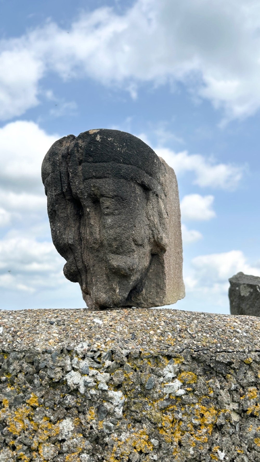 A weathered 17th-century carved stone head fragment with defined facial features and visible surface erosion. View IV