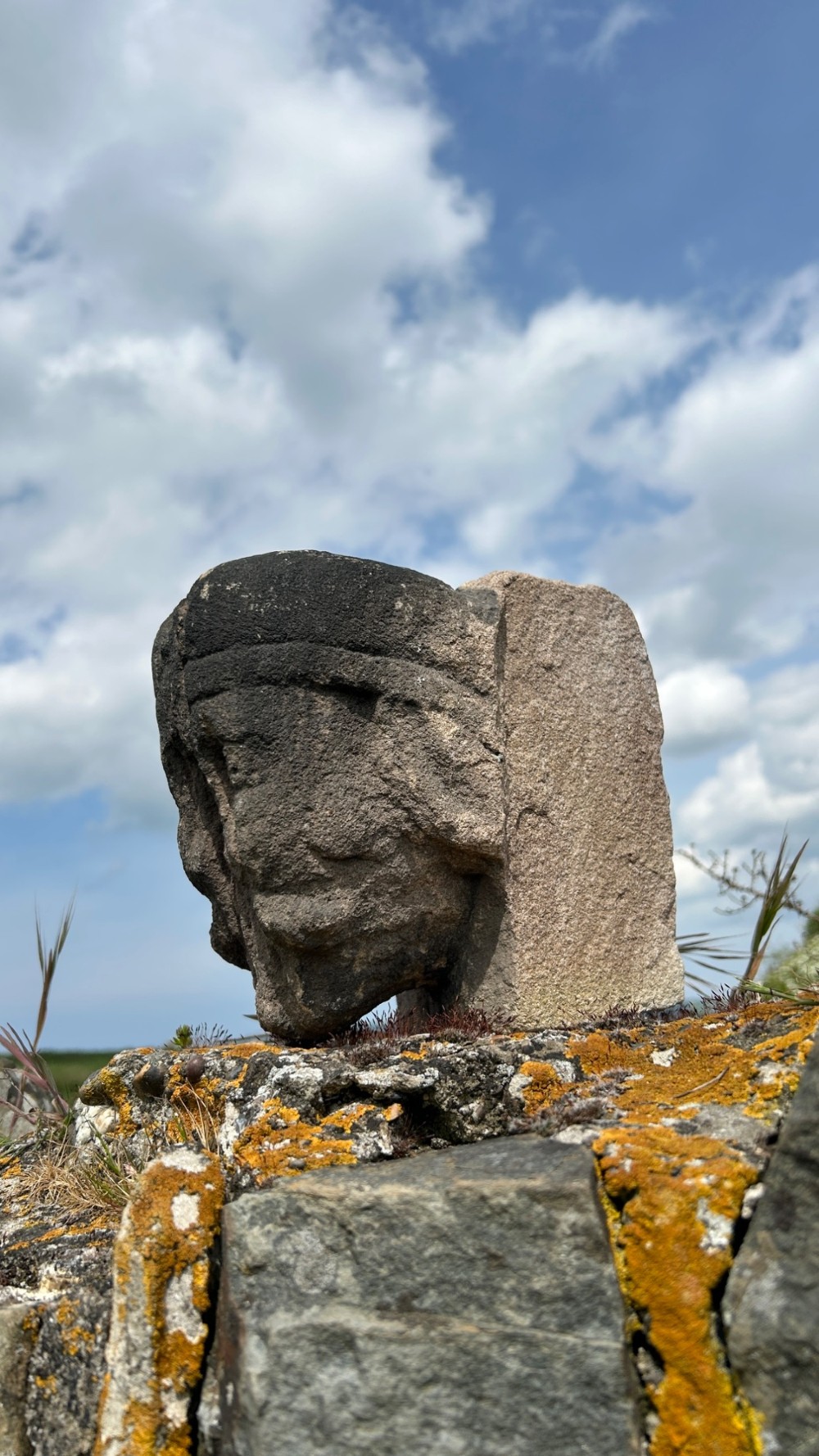 A weathered 17th-century carved stone head fragment with defined facial features and visible surface erosion. View V