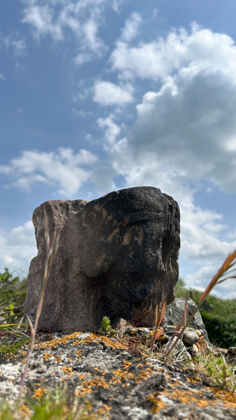 A weathered 17th-century carved stone head fragment with defined facial features and visible surface erosion. View VII