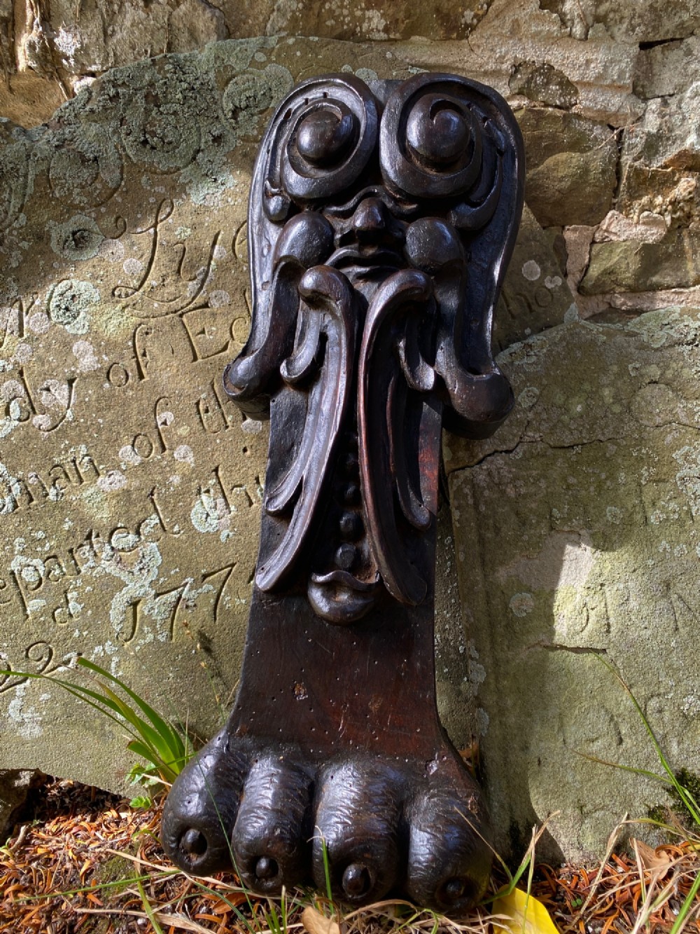 A hand-carved dark oak wood element featuring a stylised Green Man face tapering down into a lion paw base.